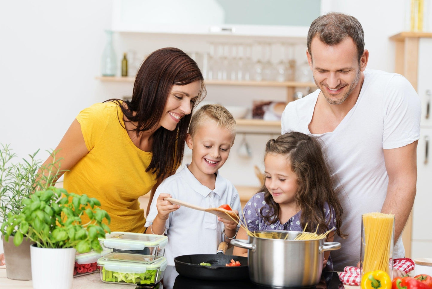 Familie mit zwei Kindern kocht gemeinsam in der Küche, mehrere FITPREP Glasbehälter mit frischem Gemüse auf dem Tisch.
